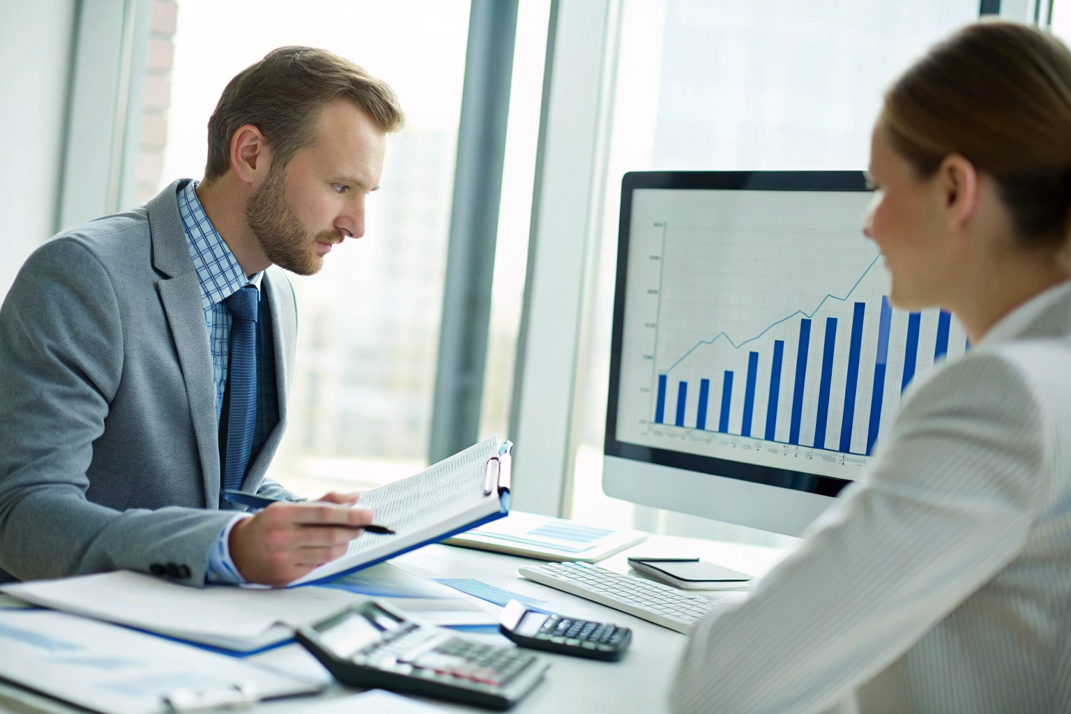 Insurance broker explaining policy costs with chart on screen in office.
