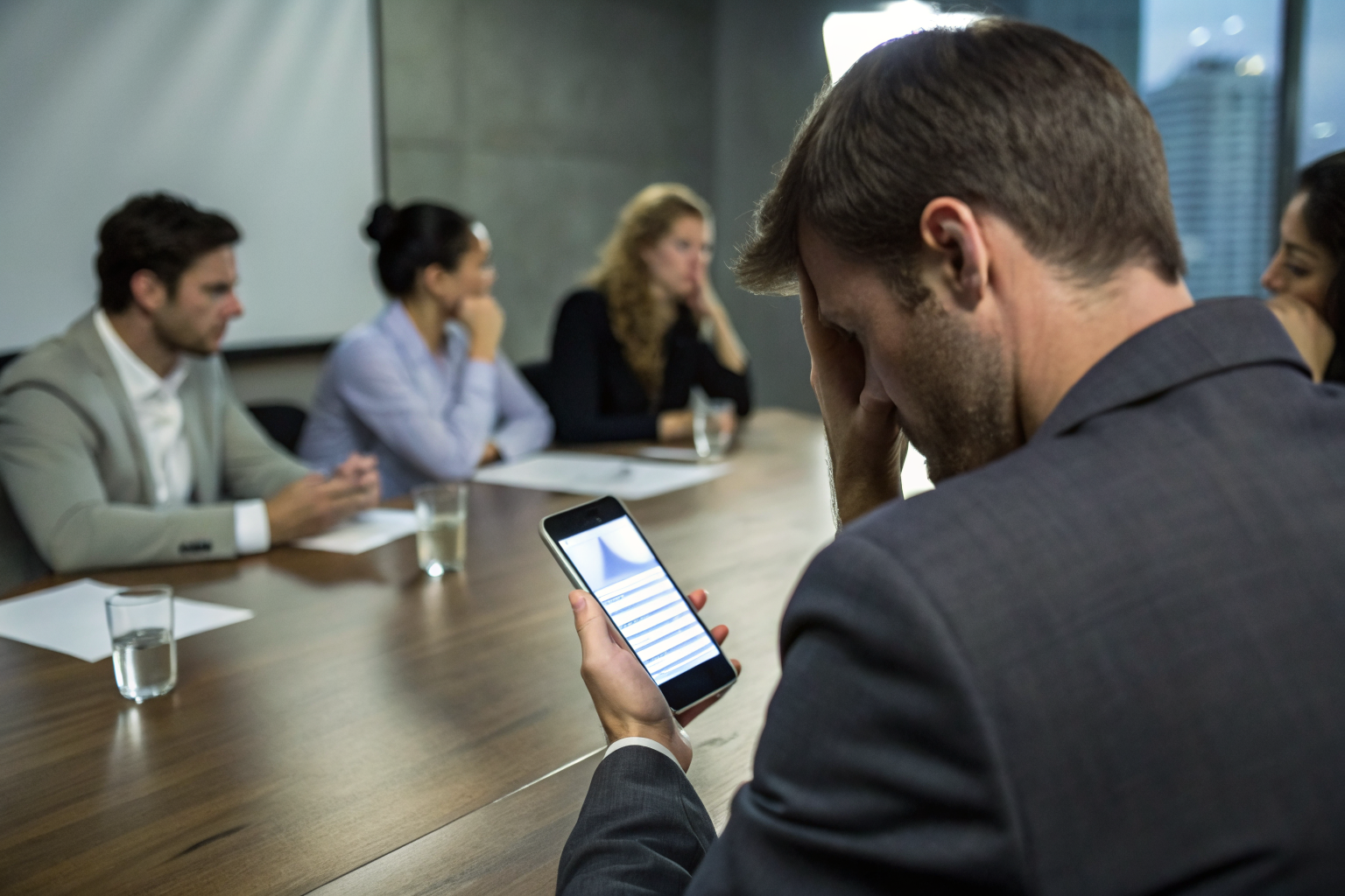 Executive showing phone with data breach notification in a boardroom.
