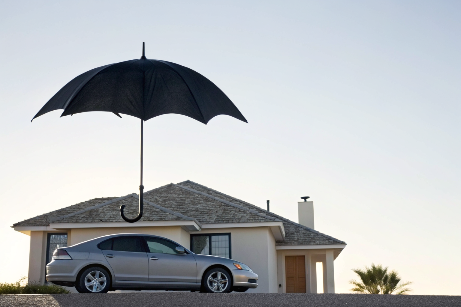 Umbrella metaphorically covering house and car, illustrating umbrella insurance.